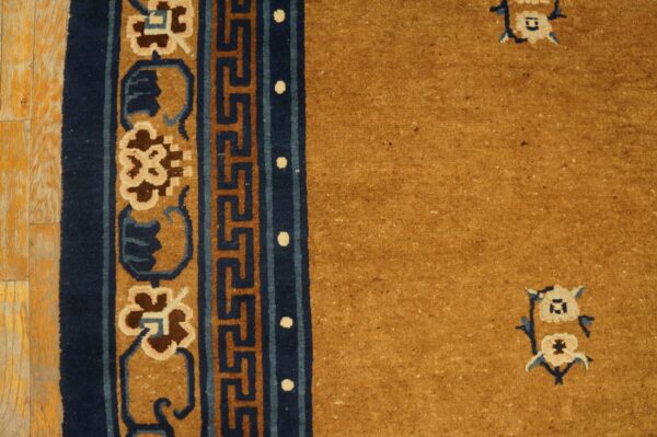 Golden yellow rug border featuring navy greek key and floral designs lies on bright hardwood flooring.