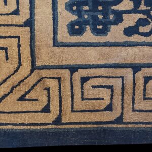 Detailed view of a rug corner showing a tan field patterned with dark blue meander and cloud motifs.