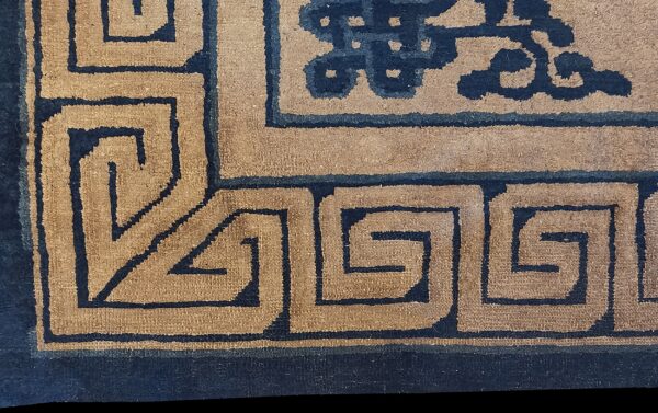 Detailed view of a rug corner showing a tan field patterned with dark blue meander and cloud motifs.