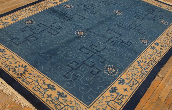 Low pile blue area rug featuring scrollwork, geometric designs, and wide floral borders on wood flooring.