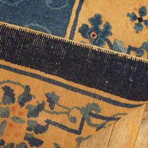 A detailed blue and camel patterned rug is folded back, highlighting the woven border on a wood floor.