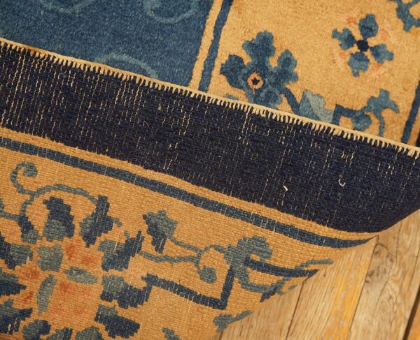 A detailed blue and camel patterned rug is folded back, highlighting the woven border on a wood floor.