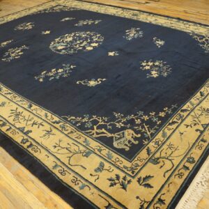 Navy blue rug with a wide tan and pale blue floral border on light wooden floorboards.
