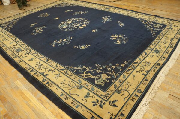 Navy blue rug with a wide tan and pale blue floral border on light wooden floorboards.