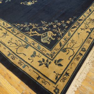 Navy blue rug corner featuring a tan border with blue floral and animal motifs on wood flooring.