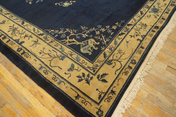 Navy blue rug corner featuring a tan border with blue floral and animal motifs on wood flooring.