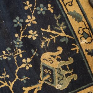 Dark blue rug detail with tan and blue-green scrolling vines, flowers, and a detailed golden border.