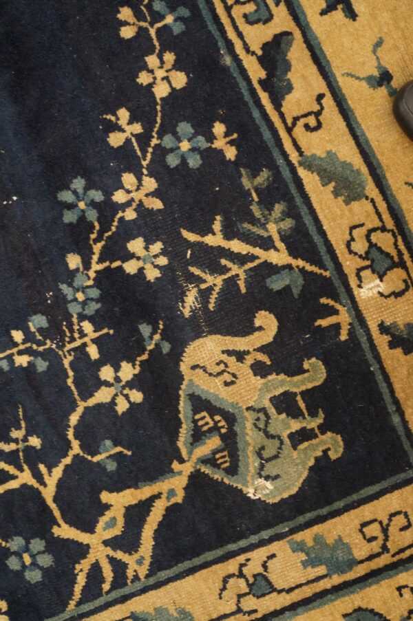 Dark blue rug detail with tan and blue-green scrolling vines, flowers, and a detailed golden border.