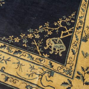 Navy blue rug corner featuring a wide mustard yellow border with teal and gold botanical motifs.