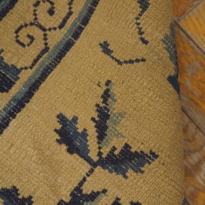 Textured mustard rug with dark blue and sage geometric patterns is shown rolled on yellow wood floor.