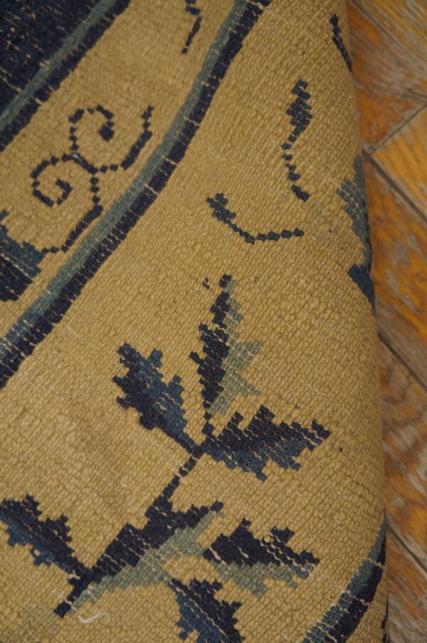 Textured mustard rug with dark blue and sage geometric patterns is shown rolled on yellow wood floor.