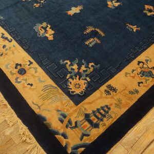 Navy rug with a wide gold border and stylized patterns rests on light wood plank flooring.