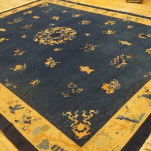 Dark blue rug with scattered gold and blue motifs, wide patterned gold border, on wood flooring.