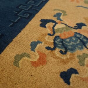 Close-up of a rug featuring an amber field, navy border, and floral motifs in blue, green, and orange.