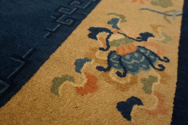 Close-up of a rug featuring an amber field, navy border, and floral motifs in blue, green, and orange.