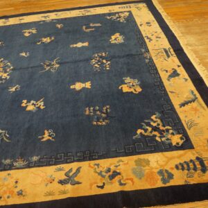 Angled view of a navy blue rug with a gold border and floral motifs on a light wooden floor.