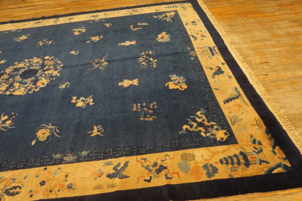 Angled view of a navy blue rug with a gold border and floral motifs on a light wooden floor.