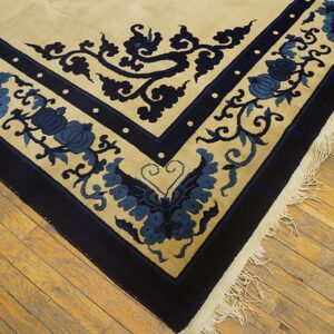 Corner view of a cream rug with blue floral and vine motifs, dark blue borders, and fringe on wood floors.
