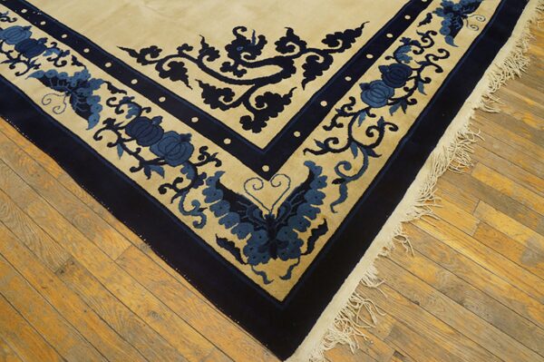 Corner view of a cream rug with blue floral and vine motifs, dark blue borders, and fringe on wood floors.