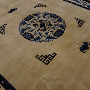 Tan rug displays dark blue border, floral medallion, and geometric corner detailing over hardwood.