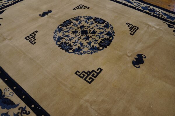 Tan rug displays dark blue border, floral medallion, and geometric corner detailing over hardwood.