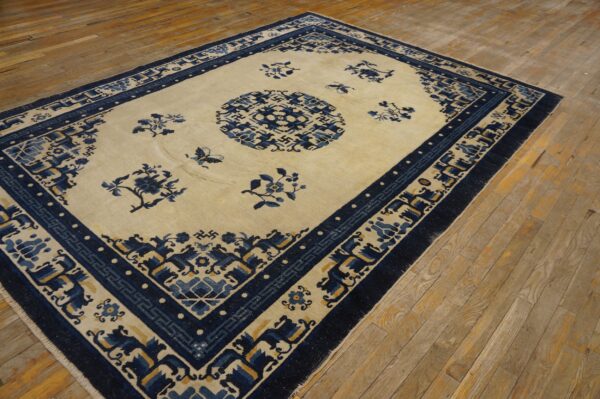 Light blue and cream rug featuring floral patterns and geometric borders on worn hardwood flooring.
