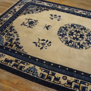 Cream and navy rug with geometric borders and floral motifs resting on distressed wooden planks.