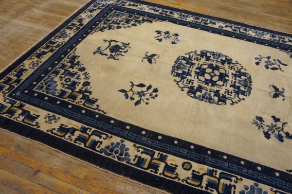 Cream and navy rug with geometric borders and floral motifs resting on distressed wooden planks.