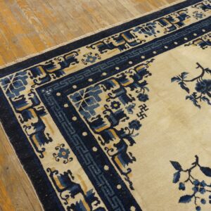 A cream and navy blue rug with floral and geometric motifs sits on distressed wood floors.