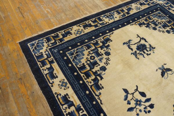 A cream and navy blue rug with floral and geometric motifs sits on distressed wood floors.