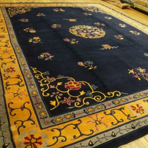 Deep blue rug with bright yellow borders and colorful floral motifs lying on light wood planks.