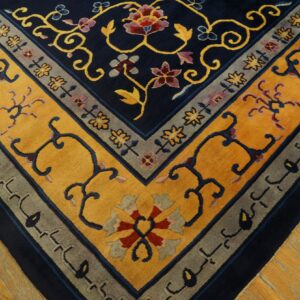 Close-up of a navy, gold, and gray floral patterned rug corner resting on light wood flooring.