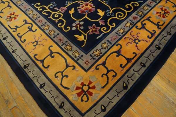 Close-up of a navy, gold, and gray floral patterned rug corner resting on light wood flooring.