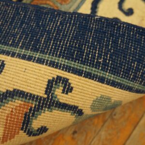 Curled rug edge detail reveals navy, beige, and rust geometric designs on a rustic wood floor.