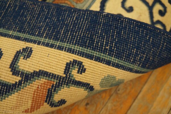 Curled rug edge detail reveals navy, beige, and rust geometric designs on a rustic wood floor.