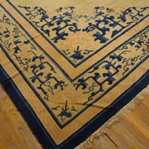 A tan rug with stylized navy blue and peach border designs lies on glossy hardwood flooring.