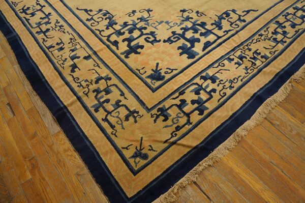 A tan rug with stylized navy blue and peach border designs lies on glossy hardwood flooring.