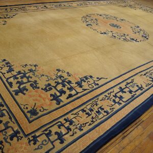 Tan rug featuring navy blue and coral borders and a medallion lies on worn wooden floorboards.