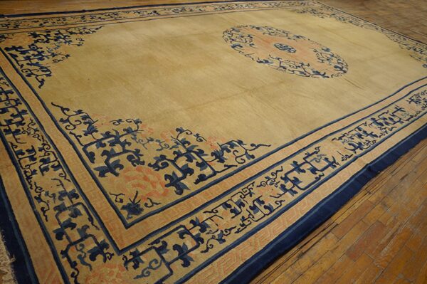 Tan rug featuring navy blue and coral borders and a medallion lies on worn wooden floorboards.