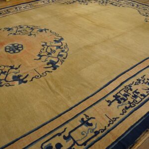 Tan rug with a large coral and navy medallion and detailed geometric border on wood flooring.