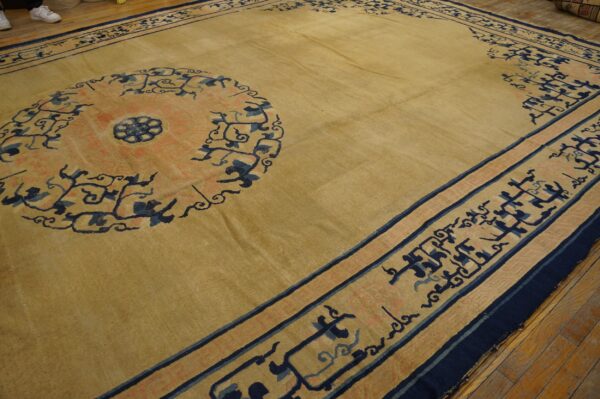 Tan rug with a large coral and navy medallion and detailed geometric border on wood flooring.