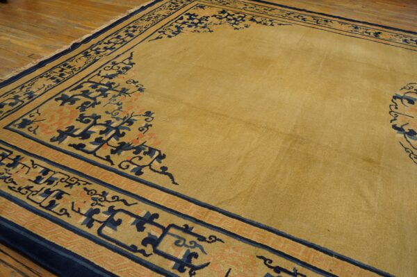Mustard yellow area rug with detailed navy and coral borders resting on rustic light hardwood floors.