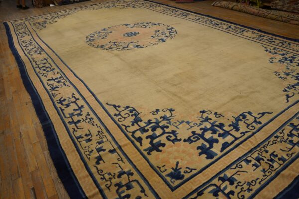 Oversize beige rug with large navy and blush circular medallion and ornate borders on wooden floor.