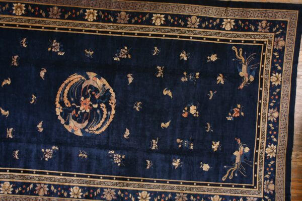 Ornate navy blue rug featuring gold phoenix motifs, scattered florals, and multiple geometric borders on hardwood.