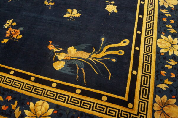 Deep navy rug featuring a gold stylized bird, geometric greek key border, and large yellow floral motifs.