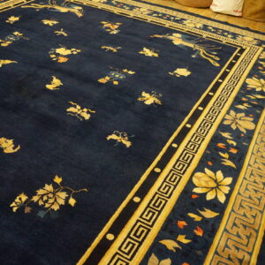 Dark blue rug with scattered yellow floral motifs and a detailed geometric border on wood floors.
