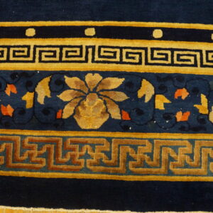 Navy blue rug featuring intricate gold and rust geometric and floral borders on hardwood flooring.