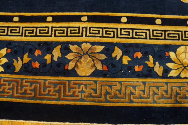 Navy blue rug featuring intricate gold and rust geometric and floral borders on hardwood flooring.