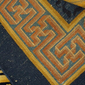 Close-up of a navy and gold geometric fret pattern rug lying on a natural wood floor.
