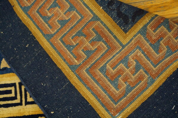 Close-up of a navy and gold geometric fret pattern rug lying on a natural wood floor.